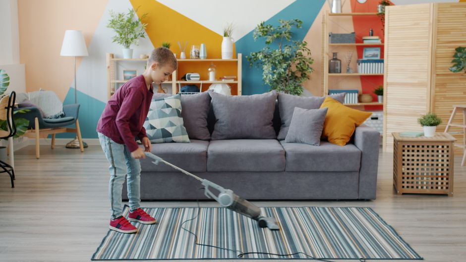 Young boy vacuuming carpet in colorful, modern living room setting.