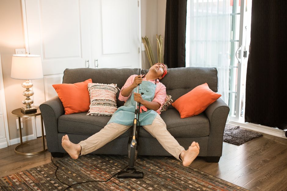 Man exhausted after vacuuming, resting on a couch with a vacuum cleaner at home.