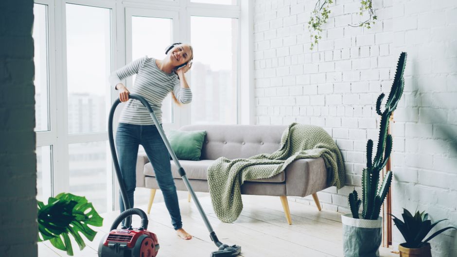 Happy woman listening to music while vacuuming a stylish living room.